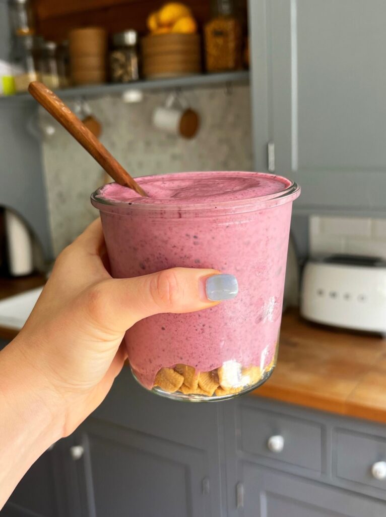 A side view of the berry cheesecake smoothie being held with a hand
